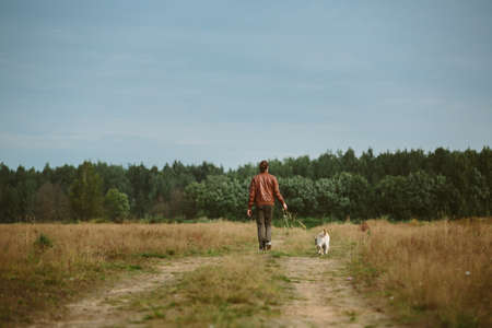 Back view of man walking with a dog on country road on a meadowの写真素材