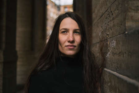 Portrait of longhair girl in black coat standing in a yard looking thoughtfully at camera.の写真素材