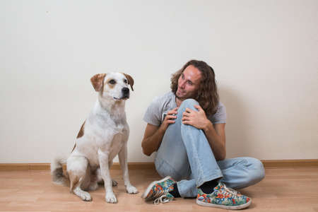 Young man is playing with his dog at home, near the wallの写真素材