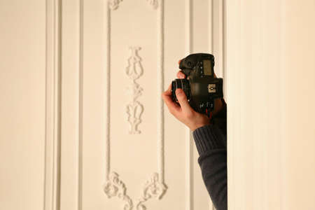 Studio shot of somebody hands behind the wall holding professional photocamera.の写真素材