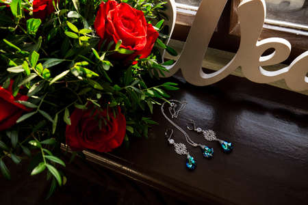 Jewelry set earrings and pendant necklace on brown windowsill. Red and green bouqet placed near.の写真素材