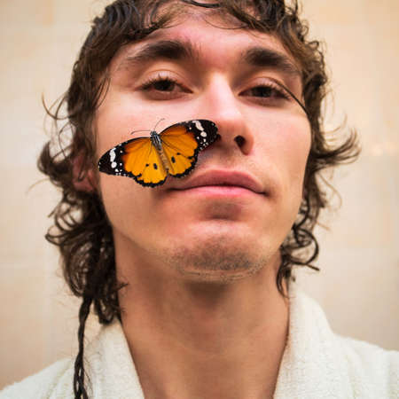 Portrait of a young man with a yellow butterfly on his cheek.