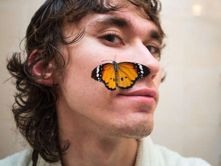 Portrait of a young man with a yellow butterfly on his cheek.の写真素材