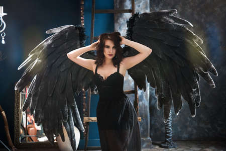 Attractive sensual woman posing in black angel costume with big wings.