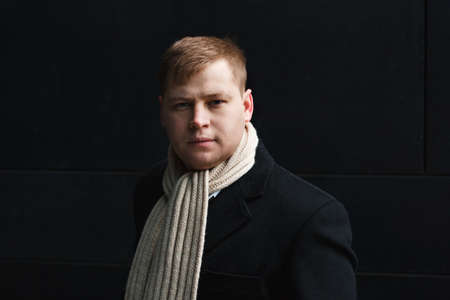 Portrait of elegant man in black coat standing on black wall background looking at camera.の写真素材