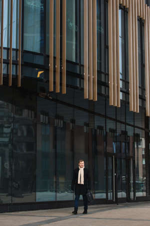 Side view of elegant man in black coat walking on sidewalk against contemporary building.の写真素材
