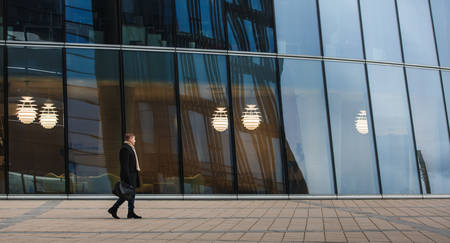 Side view of elegant man in black coat walking on sidewalk against contemporary building.
