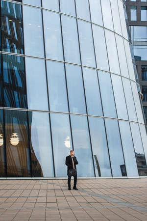 Side view of elegant man in black coat standing on sidewalk against contemporary building.の写真素材