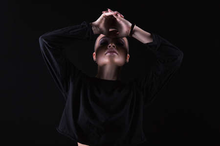 Young sensual woman with shaven head wearing black sweatshirt and posing with hands above face. の写真素材
