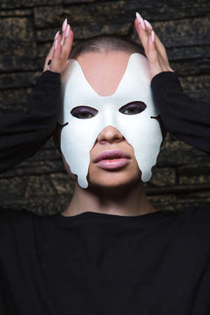 Close up portrait of an Anonymous girl with shaved head wearing black sweatshirt and white butterfly mask posing sensually.の写真素材