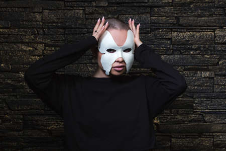 Anonymous girl with shaved head wearing black sweatshirt and white butterfly mask posing sensually.の写真素材