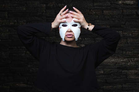 Anonymous girl with shaved head wearing black sweatshirt and white butterfly mask posing sensually.の写真素材