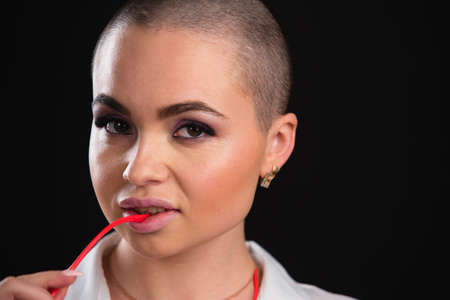 Close up portrait of a beautiful alluring model with shaved head posing nude in white shirt and glasses in studio on black backgroundの写真素材