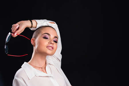 Close up portrait of a beautiful alluring model with shaved head posing nude in white shirt and glasses in studio on black backgroundの写真素材