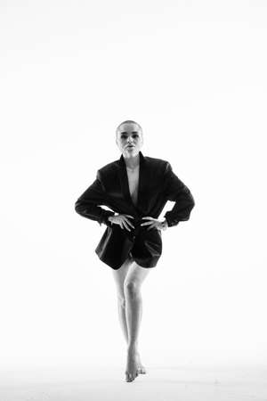 Young nude woman with shaved head covering body with short shirt looking at camera on white.の写真素材