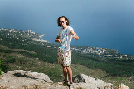 Photo of young handsome funny man standing on edge of the mountain and looking at cameraの写真素材