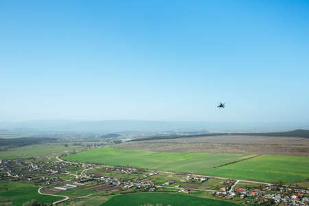 A military helicopter flying over the village. Sunny day, blue sky backgroundの写真素材