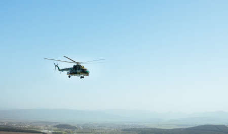 A military helicopter flying over the village. Sunny day, blue sky background