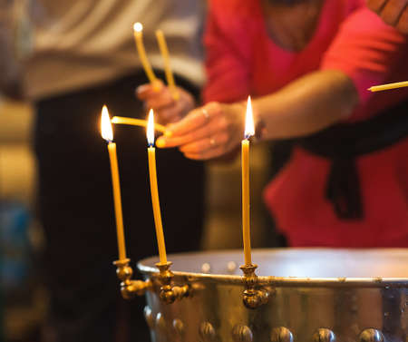 Close up view at somebody's hands set fire to a wax candle in the church