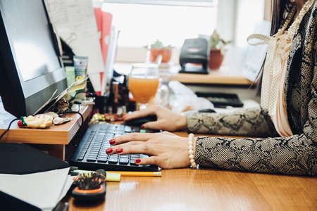 Cropped view of a female office worker. Close-up of busy female hand typing on keyboard while sitting at her working place in the officeの写真素材