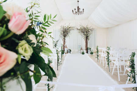 Indoor wedding ceremony with white wedding arch decorated with flowers and big white candles.の写真素材
