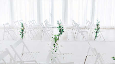 Indoor wedding ceremony with white wedding arch decorated with flowers and big white candles.の写真素材