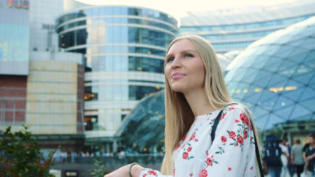 Amazed woman in modern city. Young lady in elegant outfit admiring view in astonishment while standing on background of futuristic building on street of modern city.の写真素材