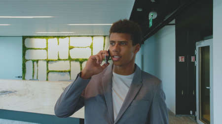 Handsome African-American man in suit having phone call in office looking confidently awayの写真素材