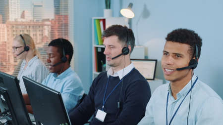 Cheerful customer support agent of mixed ethnicity talking on phone with a headset. He working in modern call center office.の写真素材