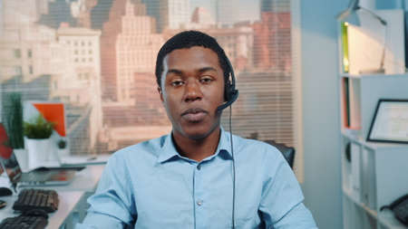 Black customer service operator talking to client in call center with skyscrapers in the background.