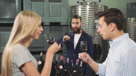 People degustation wine with sommelier. Bearded sommelier showing how to taste wine correctly to young visitors of viticulture production.の写真素材
