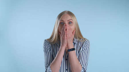 Blonde female widely opening her mouth in astonishment. Blue background.の写真素材