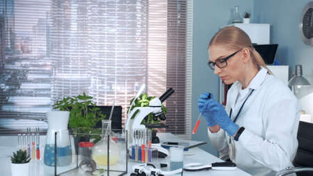 In modern research laboratory: female scientist using pipette to drop sample on slide and looking into microscope. There are different instruments and lab hamster on her table.の写真素材