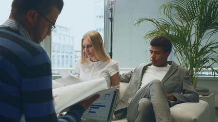 Group of diverse men and woman sharing papers and working with laptop in modern office having meetingの写真素材