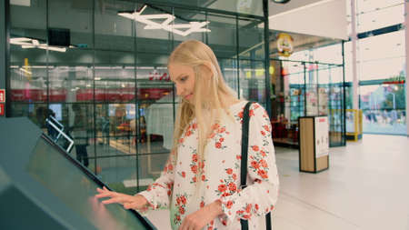 Woman near navigation board in mall. Side view of lovely young female in casual outfit looking for right direction on navigation board in modern mall.の写真素材