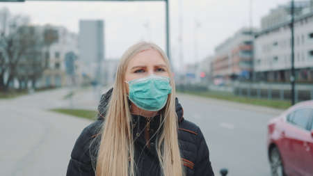 Concerned woman in medical coronavirus mask walking on the street. City buildings and road on the background. Coronavirus pandemic concept.の写真素材