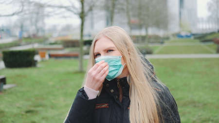Young female feeling saved by putting on face medical mask. She standing in the city center. Coronavirus pandemic concept.の写真素材