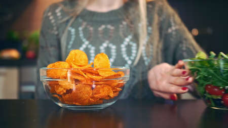 Close-up shot of lady preferring crisp to salad. Attractive young woman choosing to eat healthy...