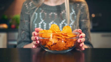 Young lady preferring crisp. Attractive young woman choosing to eat healthy crisp for lunch while sitting at table in stylish kitchen.の写真素材