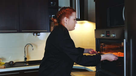 Bakery worker putting oven-tray with cookies to the oven. Woman making gingerbread cookies.