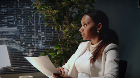 Beautiful african american business woman explaining the text of contract in office. There are skyscrapers in the background.の写真素材