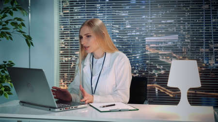 Female psychologist in white coat making online video consultation with patient on computer sitting...