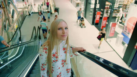 Woman riding escalator in mall. From below shot of lovely young lady looking up while riding moving staircase in modern mall in Asia.の写真素材