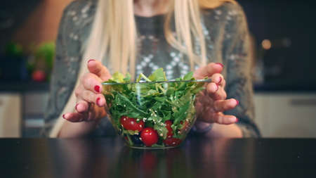 Young lady preferring salad. Attractive young woman choosing to eat healthy salad for lunch while sitting at table in stylish kitchen.の写真素材