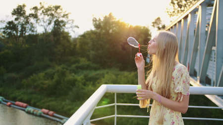 Woman blowing soap bubbles. Side view of pretty woman blowing soap bubbles while standing on pedestrian bridge.の写真素材