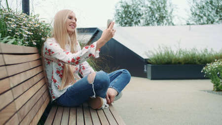 Woman making video call on green roof. Lovely young female using smartphone to make video call while...