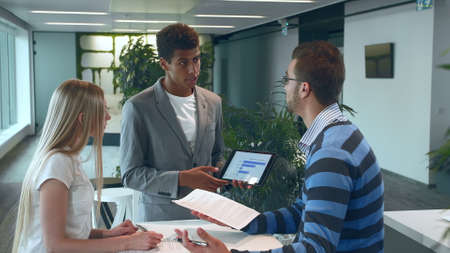 Group of diverse woman and men with tablet in modern office hall having work with documents and statistics.の写真素材