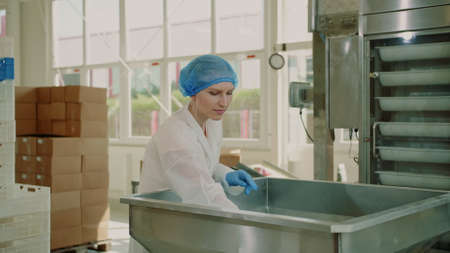 Candy factory. Factory worker checking packing machine. Young woman in uniform inspecting packing machine while working in confectionery factory.の写真素材