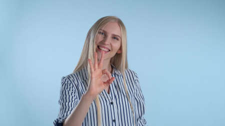 Attractive blonde woman making okay hand sign. She making hand gesture on blue background.の写真素材