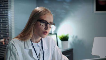 Close-up of female psychologist in eyeglasses and lab coat making video call with patient by computer and giving important advices in modern officeの写真素材